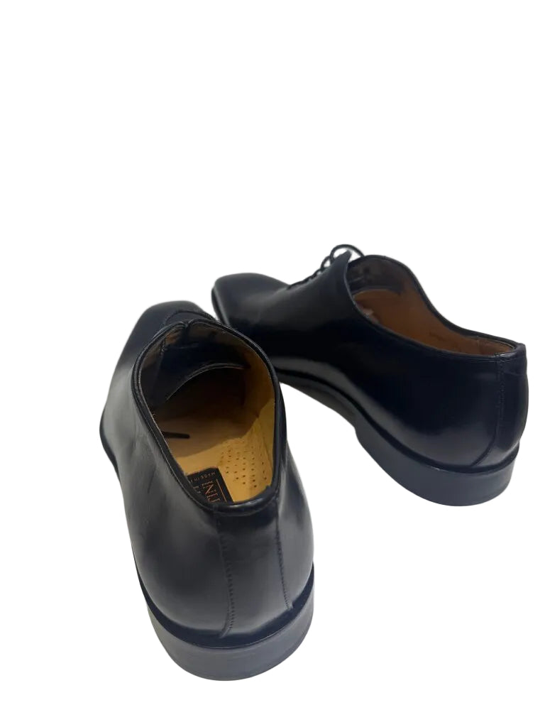 Pair of black dress shoes on a white platform with a white background