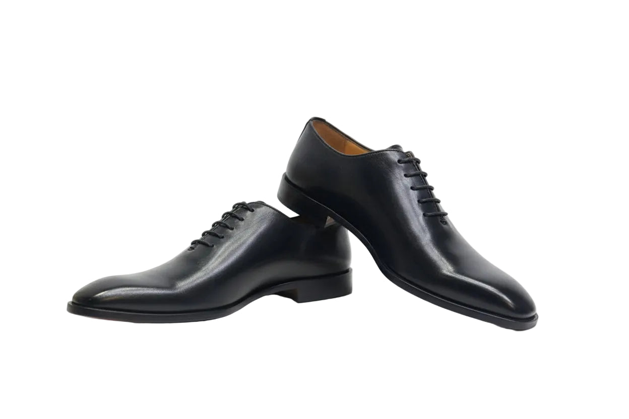 Black leather dress shoes with brown soles on a white background
